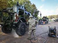 A serviceman in full CBRN protection cleans a vehicle