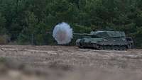 Ein Kampfpanzer Leopard 1 A5 schießt im Gelände. Eine Rauchwolke kommt aus dem Rohr.