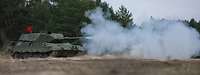Ein Panzer schießt im Gelände. Aus dem Rohr kommt weißer Rauch.