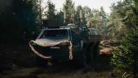 Ein Radpanzer mit Antennen auf dem Dach steht im Wald.