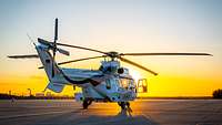 Ein Hubschrauber steht während eines Sonnenuntergangs auf dem Rollfeld.
