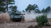 Ein Kampfpanzer fährt im Gelände und wirbelt Staub auf.