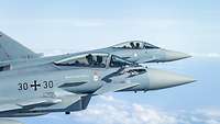Zwei Eurofighter fliegen bei blauem Himmel Seite an Seite.