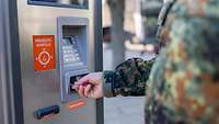 Ein Soldat steckt seine Kreditkarte in einen Kassenautomaten.