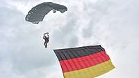 Ein Soldat hängt mit einer Deutschlandfahne an einem Fallschirm in der Luft.