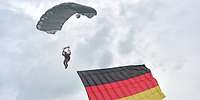 Ein Soldat hängt mit einer Deutschlandfahne an einem Fallschirm in der Luft.