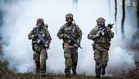 Drei Soldaten mit Ausrüstung gehen nebeneinander vor einer Nebelwand auf den Betrachter zu.