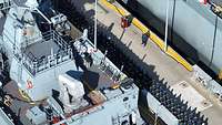 Luftaufnahme: Zwischen zwei Kriegsschiffen stehen angetretene Soldaten auf der Pier.