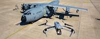 Eine Drohne schwebt vor einem militärischen Transportflugzeug.