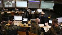 Mehrere Soldaten überwachen in einem Raum die Systeme und Netze auf einer Übung. 