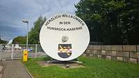 Ehemalige Antenne der Bodenstation vor der Kaserne mit dem Schriftzug "Herzlich Willkommen in der Hunsrück-Kaserne" 