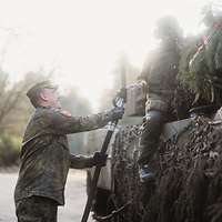 Ein Soldat reicht einem anderen Soldaten, der auf einem Panzer sitzt, eine Zapfpistole hoch.