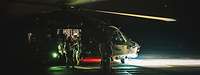 Military personnel in front of a helicopter in the dark