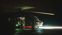 Military personnel in front of a helicopter in the dark