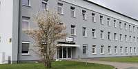 Dreistöckiges, längliches, hellgraues Gebäude wie ein Wohnblock