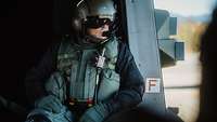 Ein Soldat sitzt in der Kabine eines Helikopters. Die Schiebetür der Kabine ist offen.
