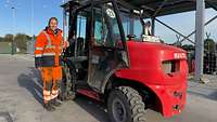 Eine Frau in Arbeitskleidung steht an einem Gabelstapler.