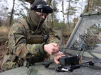 Auf der Motorhaube eines Fahrzeugs befestigt ein Soldat den Akku an einer Drohne
