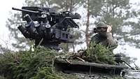 In einem Wald blickt ein stehender Soldat aus der Luke eines getarnten GTK Boxer
