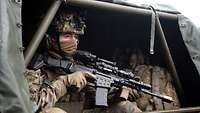 Aus dem hinteren Bereich eines Gefechtsfahrzeugs blickt ein sitzender Soldat mit einer Waffe