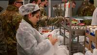Militärangehörige in Uniform sowie eine Zivilistin in Hygieneschutzuniform packen ihre Lunchpakete