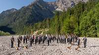 Das Gebirgsmusikkorps der Bundeswehr steht in einem ausgetrockneten Kiesbett dahinter die Alpen