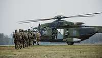 Mehrere Soldaten laufen hintereinander auf einen Hubschrauber zu.