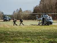 Drei Hubschrauber und mehrere Soldaten auf einer Wiese am Waldrand