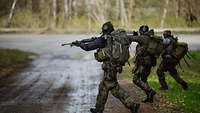 Drei Soldaten mit ihren Waffen im Anschlag laufen nebeneinander im Gelände.