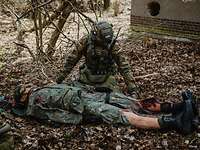 Ein Soldat kniet am Boden und versorgt eine Puppe mit einer Beinverletzung.