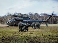 Soldaten tragen ihre Ausrüstung und verwundete Personen über eine Wiese zu einem Hubschrauber.