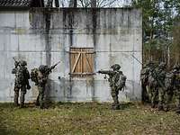 Soldaten mit Waffen bewegen sich an einem Gebäude.