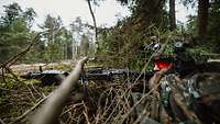 Ein mit Zweigen getarnter Soldat liegt mit Maschinengewehr im Gebüsch.