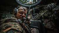 Ein Soldat mit Headset sitzt in einem Panzer schaut in die Kamera.