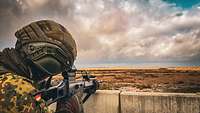 Ein Soldat steht hinter einer Mauer mit einem Sturmgewehr im Anschlag.