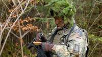 Ein Soldat in Kampfanzug mit getarntem Schutzhelm schreibt auf seinem Meldeblockzettel.