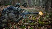 Ein Soldat liegt im Wald auf dem Boden und schießt. Neben ihm liegt ein anderer Soldat.
