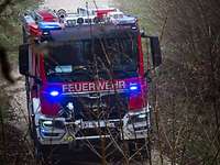 Ein Feuerwehrfahrzeug fährt mit Blaulicht auf einer unbefestigten Fahrbahn.