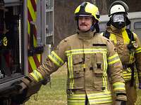 Zwei Feuerwehrmänner am Heck eines Feuerwehrfahrzeuges. Einer trägt eine Atemschutzmaske.