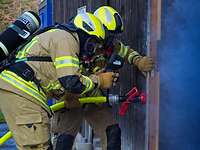 Zwei Feuerwehrleute mit Atemschutz öffnen eine Schiebetür, aus der Rauch dringt. 