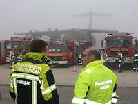 Zwei Männer vor Feuerwehrfahrzeugen, dahinter die Attrappe eines Transportflugzeuges