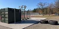 Dunkelgrüner Metallcontainer mit Metallgerüsten und großen Reifen im Freien