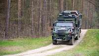 Ein gepanzertes Militärfahrzeug mit Rotem Kreuz fährt im Gelände einen Hügel hinunter.