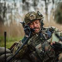 Ein Soldat spricht in ein Handset eines Funkgerätes im Gelände.