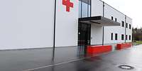 Weißes Gebäude mit einem großen Roten Kreuz links oberhalb des Eingangs