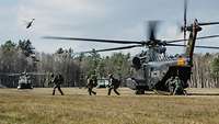 Soldaten mit Ausrüstung verlassen einen Hubschrauber und laufen über eine Wiese.