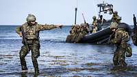Bewaffnete Soldaten stehen knietief im Wasser. Im Hintergrund sind Soldaten im Schlauchboot zu sehen.
