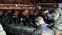 Mehrere Soldaten sitzen um einem Tisch mit einer Geländekarte. Ein Ausbilder steht vor ihnen.