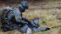 Ein Soldat hockt neben einem liegenden Soldaten und untersucht ihn.