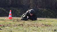 Ein Soldat robbt über eine Wiese, links von ihm ein Warnkegel.